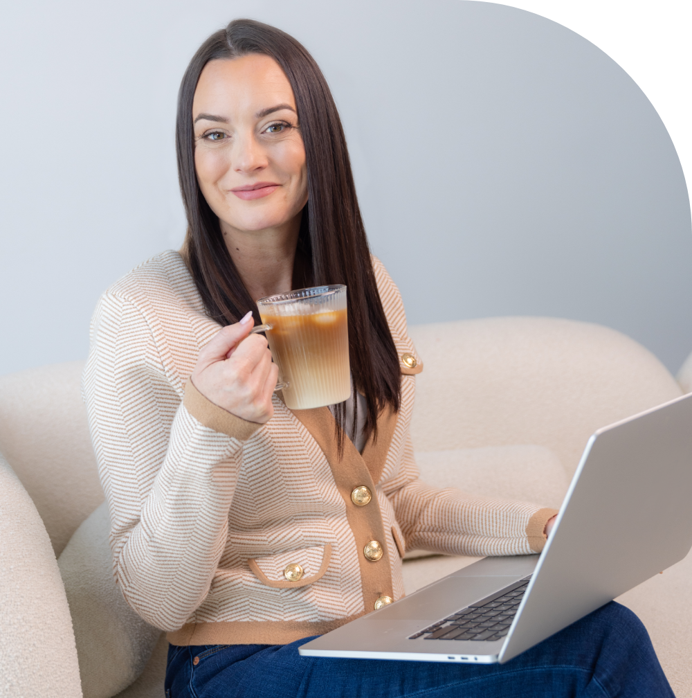 Amber Olson Rourke smiling with a cup of coffee in one hand and her laptop on her lap.